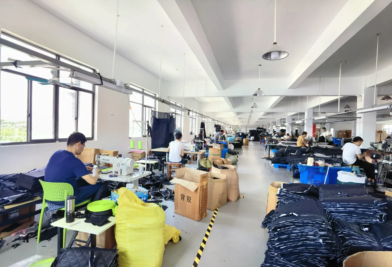Textile sewing workstations with workers and pet product components in a manufacturing workshop